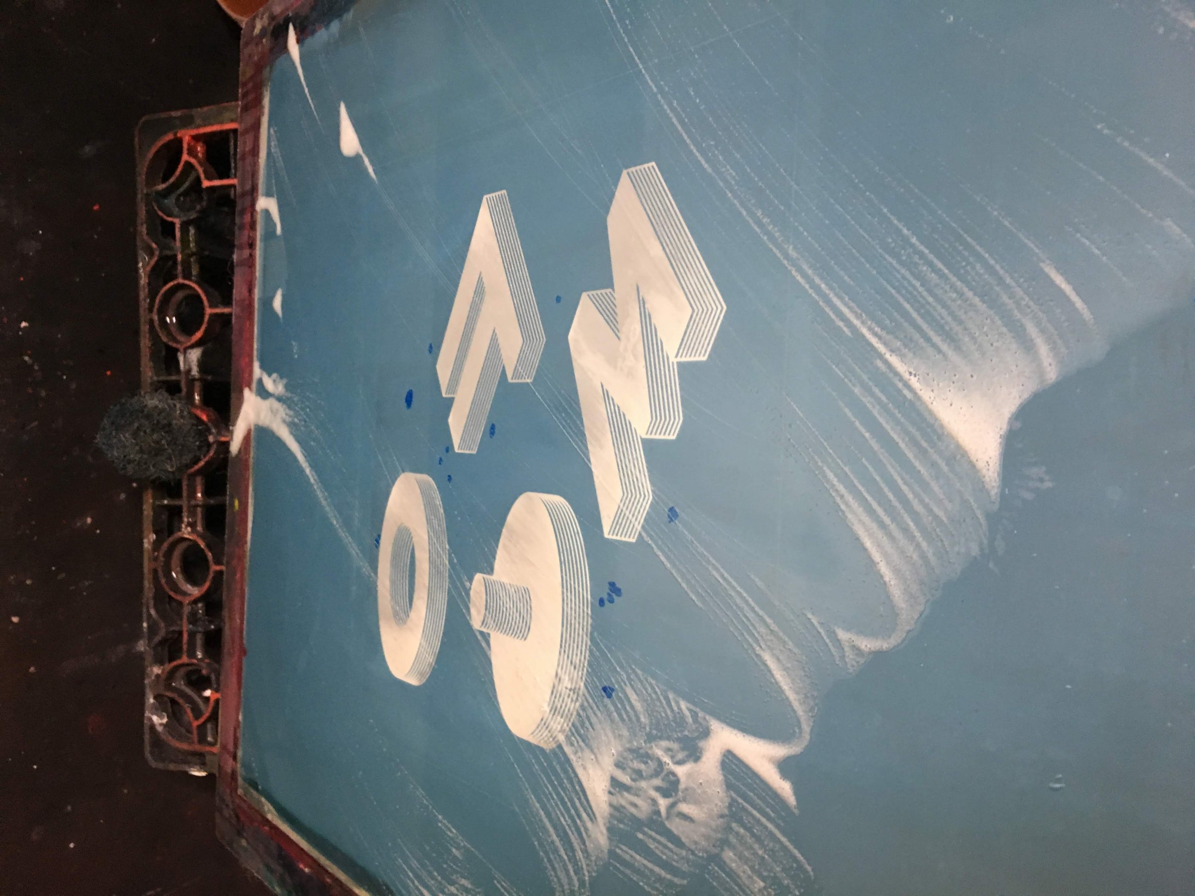 The FOMO screen being cleaned, the isometric letters showing through the blue emulsion under streaks of foam.