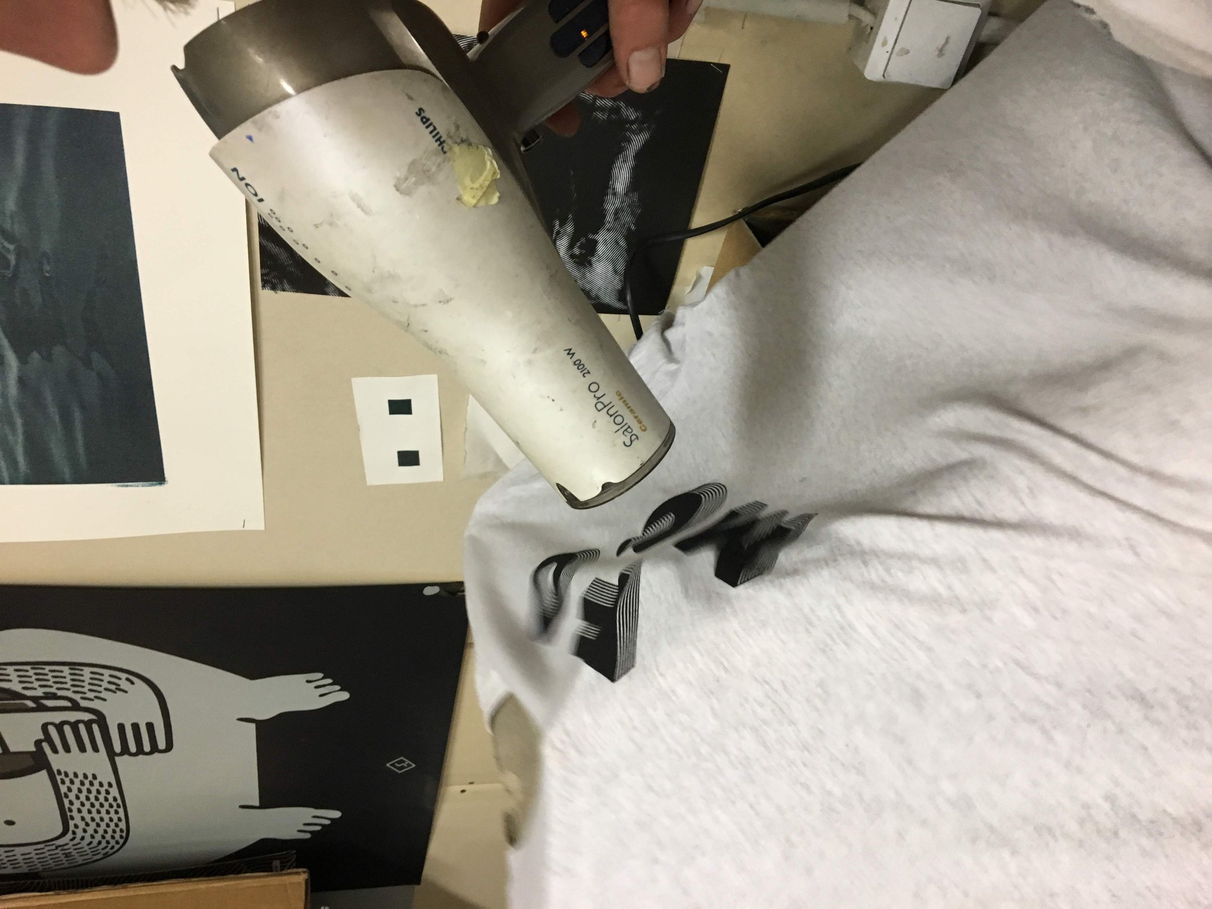 Drying a fresh FOMO print on a grey sweatshirt with a hair dryer.